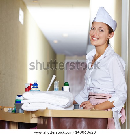 Happy cleaning lady with cleaning cart doing housekeeping in hotel