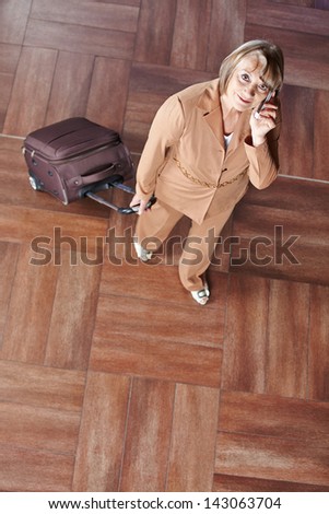 Senior woman pulling her suitcase and making phone call with her smartphone