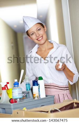 Happy hotel maid behind cleaning cart in hotel corridor