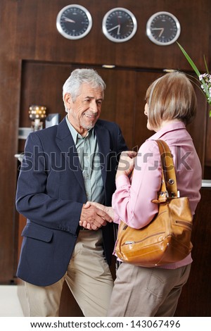 Two senior people meet at hotel reception and shaking hands