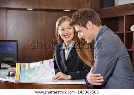 Smiling receptionist in hotel helping a guest with a city map