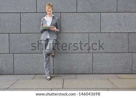 Business woman with tablet computer in the city leaning on a wall