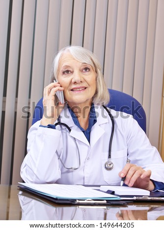 Senior doctor making phone call with smartphone in hospital office