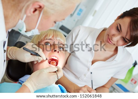 Dentist giving dental treatment with probe and mirror and dental assistant watching