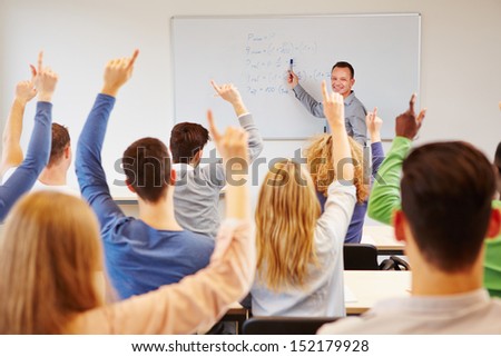 Students lifting hands in college class with teacher on whiteboard