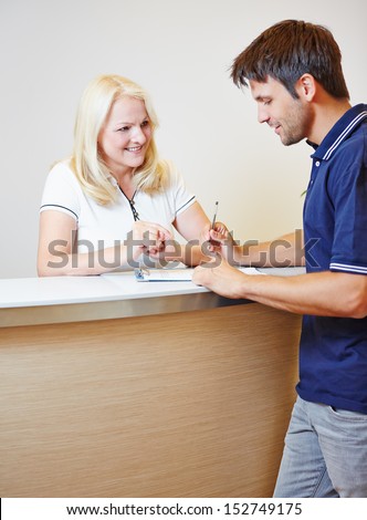 Patient filling out a form at the reception with doctors assistant