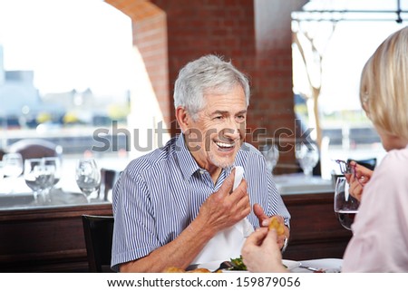 Happy elderly man cleaning his mouth with napkin at a restaurant