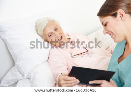 Geriatric nurse reading book to senior citizen woman in bed