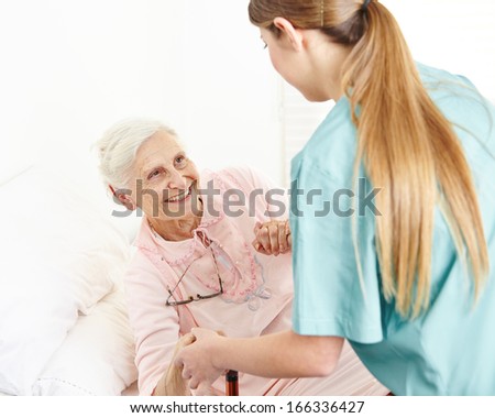 Nurse at extended home care helping smiling senior woman out of bed