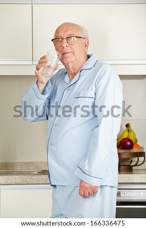 Senior man in his pajamas drinking a glass of water in the kitchen