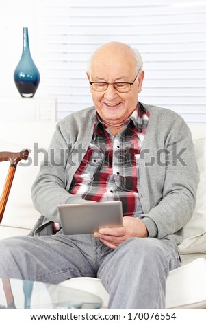 Old senior man using tablet computer to surf the internet at home