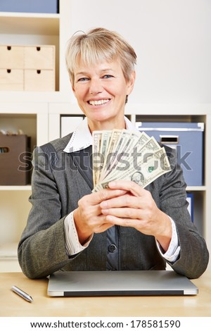 Elderly happy business woman with fan of dollar bills in the office