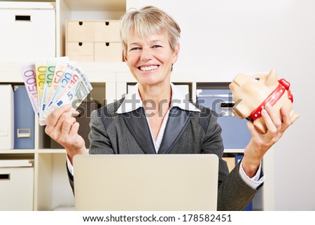Happy senior business woman in her office with Euro money and a piggy bank