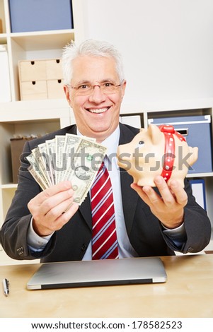 Smiling elderly business man with dollar bills and piggy bank in the office