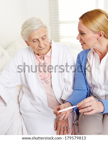 Geriatric nurse with fever thermometer and senior patient at home
