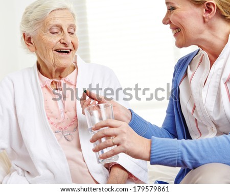 Senior woman taking pill with water from geriatric nurse