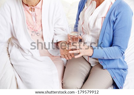 Senior citizen woman getting pill with water from a nurse