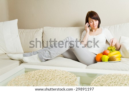 Happy young woman on her mobile phone in the living room eating fruits