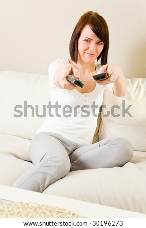 Young happy woman with two remote controls on a sofa in her living room