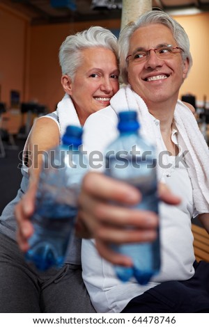 Two happy senior people in a gym drinking water