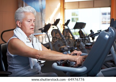 Senior woman with grey hair on home trainer in gym