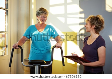 Trainer with eldery woman on treadmill in gym