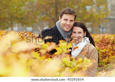Happy smiling couple behind hedge in a fall park