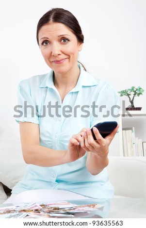 Woman with money bills using calculator in living room