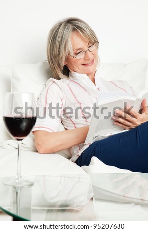 Relaxed senior woman reading a book with glass of wine