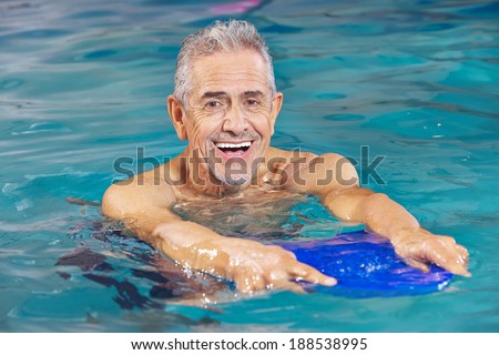 Happy senior man with kickboard in water of swimming pool