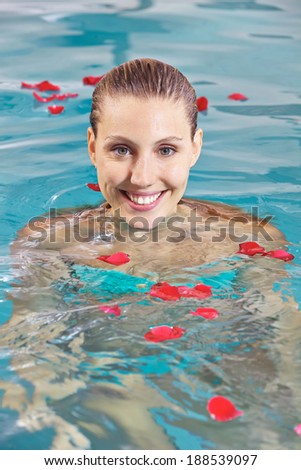Attractive young woman bathing in swimming pool with leaves of roses