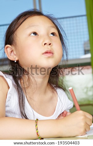 Asian girl drawing in kindergarten with pen on paper