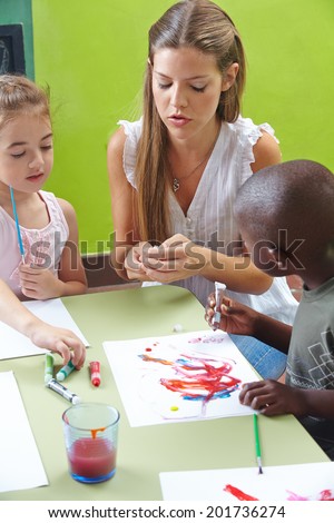 Children painting with tempera color in kindergarten and a nursery teacher is helping