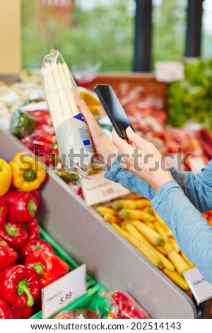 Customer in supermarket scanning barcode of a package asparagus with his smartphone