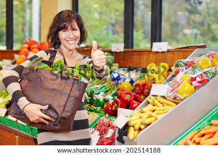Smiling elderly woman in organic food store holding her thumbs up