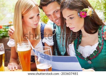 Friends looking together at drinks menu in beer garden in Bavaria