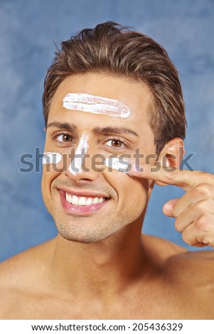 Happy young man treating his face with skin lotion