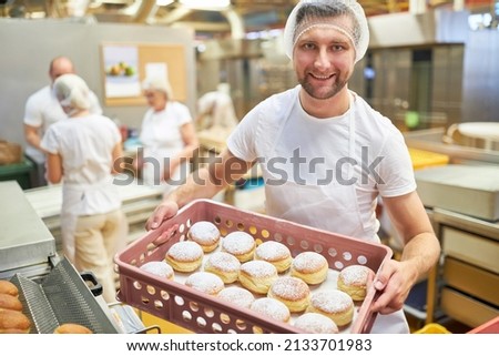 Satisfied young man as a baker apprentice carries fresh Berlin pancakes in the bakery 商業照片 © 