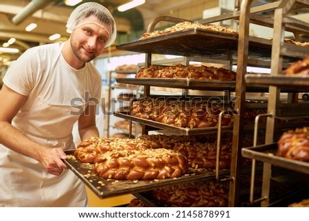 Young baker apprentice shows a baking tray with fresh yeast loaf with almonds in the bakery 商業照片 © 