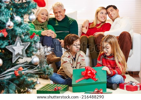 Happy children opening gifts at christmas while parents and grandparents are watching