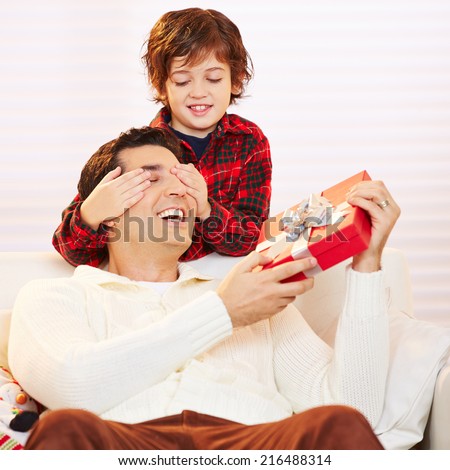 Son holding eyes of father with gift closed at christmas