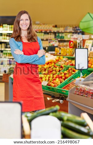 Smiling elderly saleswoman standing in a supermarket with her arms crossed
