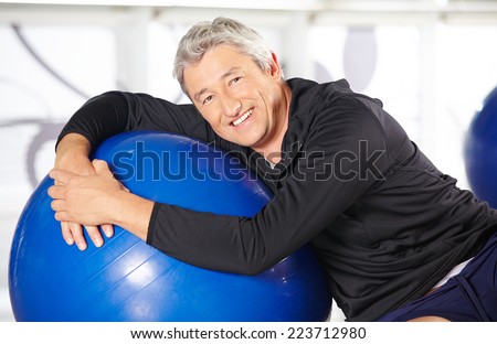 Smiling elderly man sitting with an exercise ball in a gym