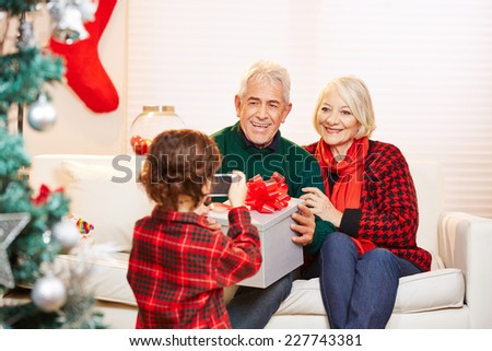 Grandchild taking photo of grandparents with smartphone at christmas