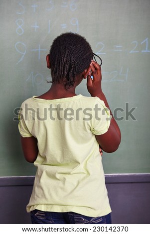 African girl solving math problem at blackboard in school