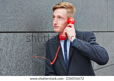 Business man making call with red phone on wall in a city