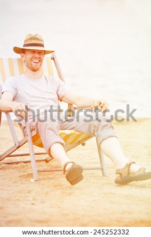 Happy relaxed Man sitting smiling in deck chair in summer on a beach