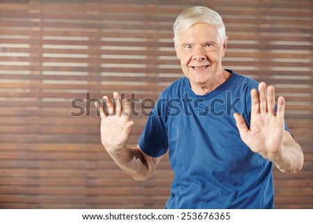 Old man doing gymnastics in fitness center and moving his hands