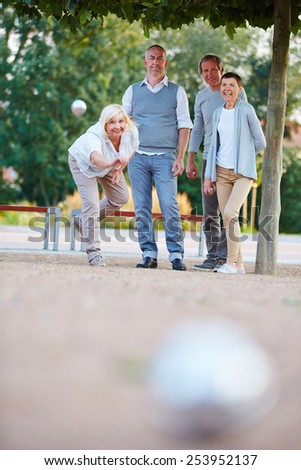Woman throwing ball while playing boule game with senior people