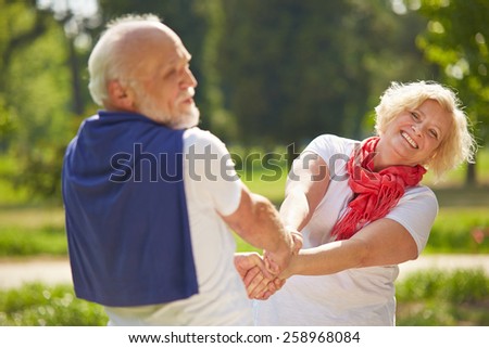 Old man and senior woman dancing together in a garden in summer